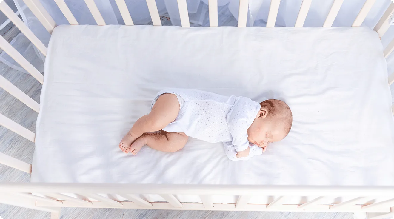 newborn baby sleeping on side in crib