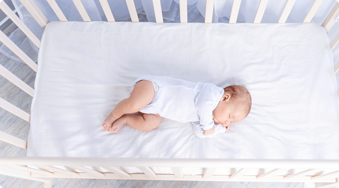 newborn baby sleeping on side in crib