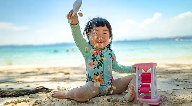 Happy toddler girl plays with a toy in the sand at the beach. 