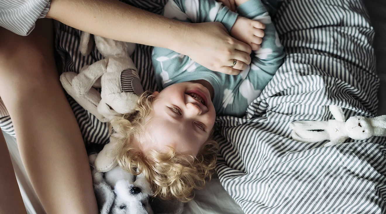 mom playing with laughing toddler in bed at home