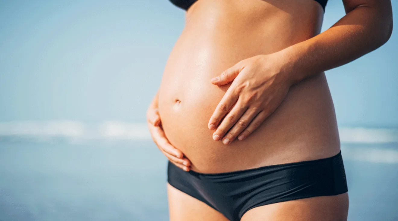 close up of a pregnant woman in a bikini on the beach during summer