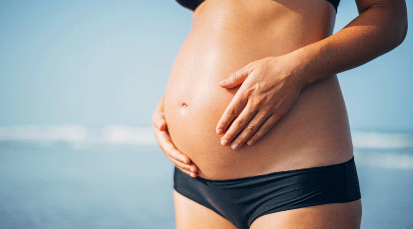 close up of a pregnant woman in a bikini on the beach during summer