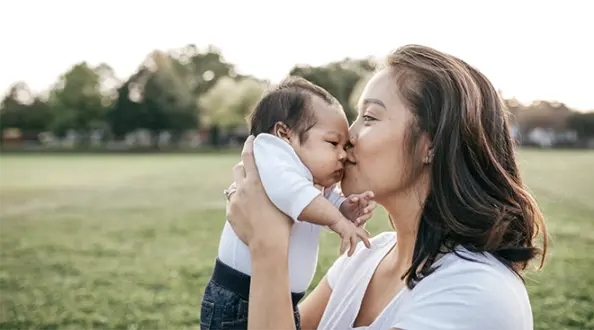 mother kissing baby's face while sitting on grass outside