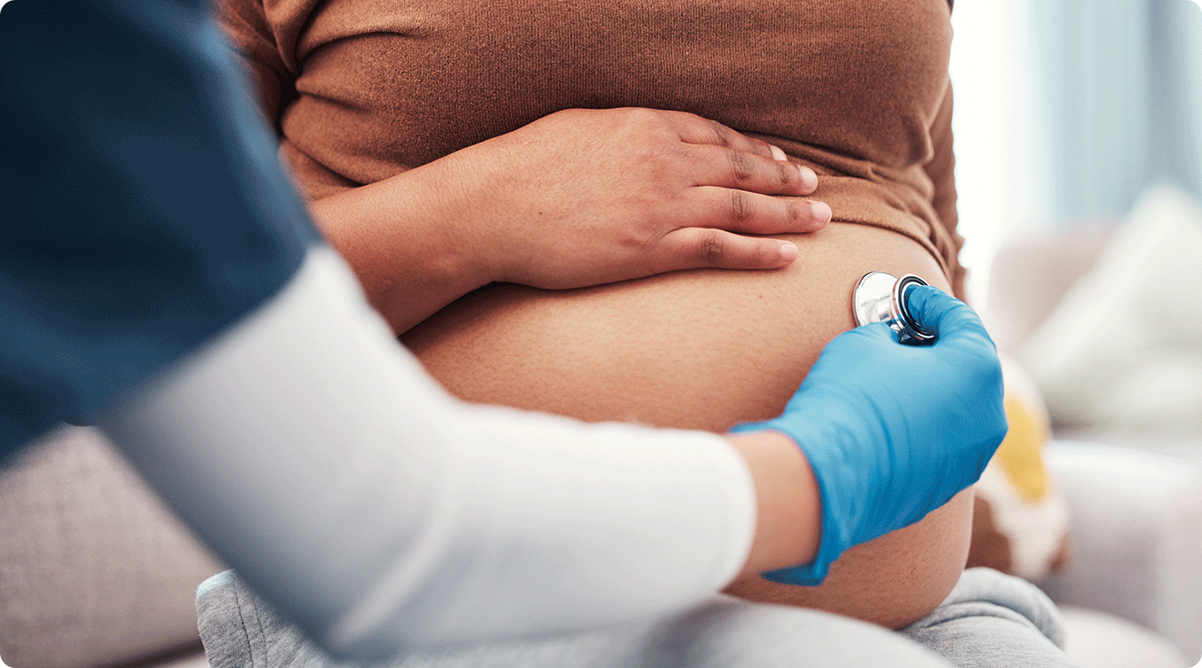 close up of nurse checking pregnant belly with stethoscope at OBGYN appointment