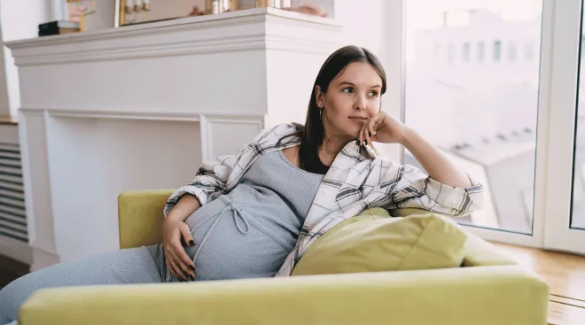optimistic pregnant woman sitting in chair at home