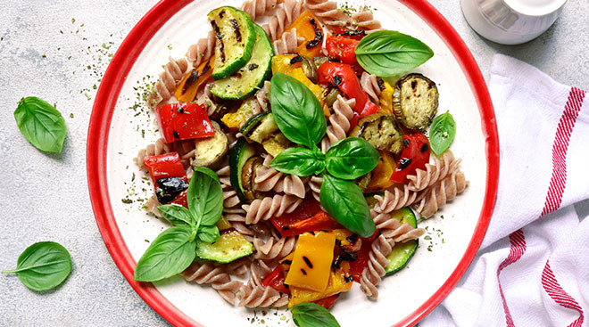 Whole wheat pasta with vegetables on a dinner plate. 
