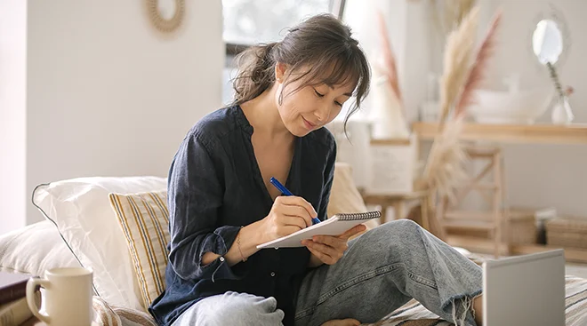 young woman writing in journal at home on the couch