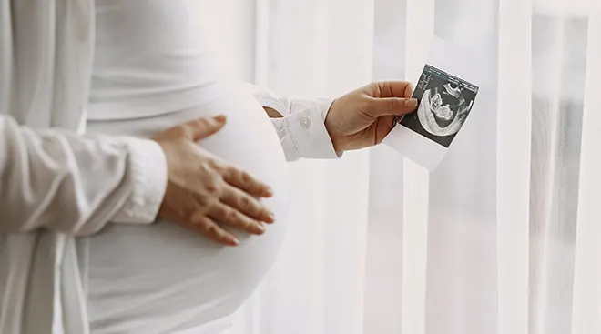 close up of pregnant woman holding ultrasound picture 