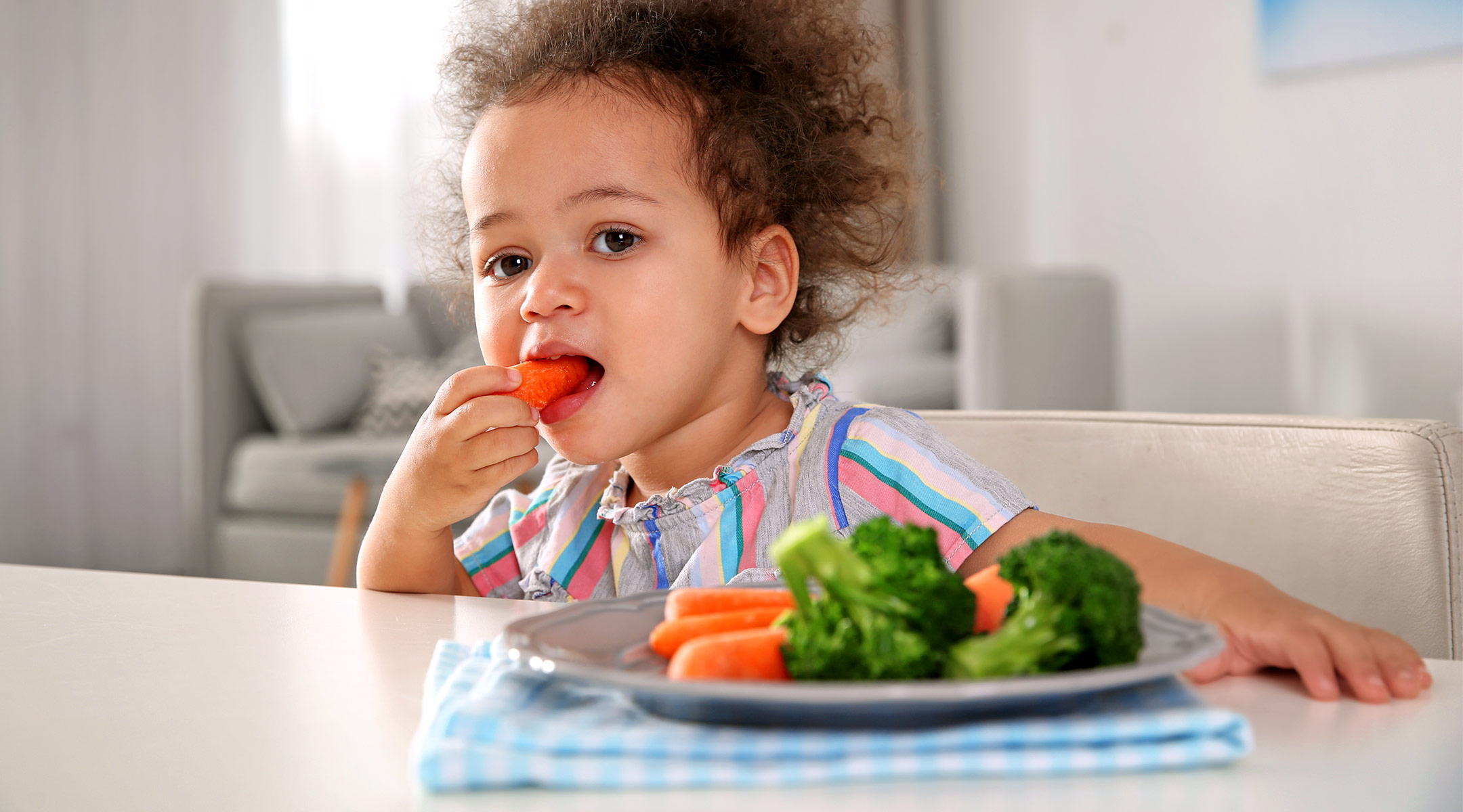 toddler eating a healthy snack, carrots and broccoli 