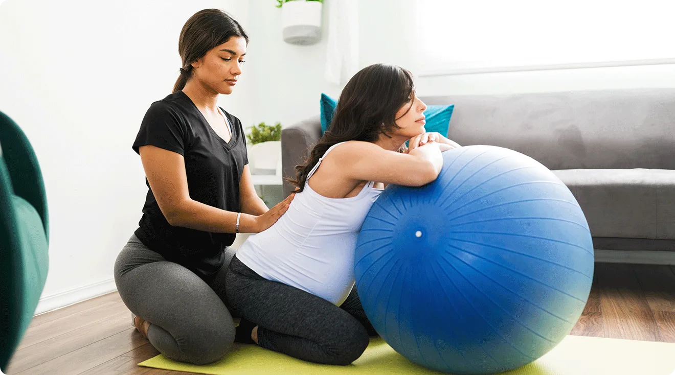 doula helping pregnant woman at home with exercise ball