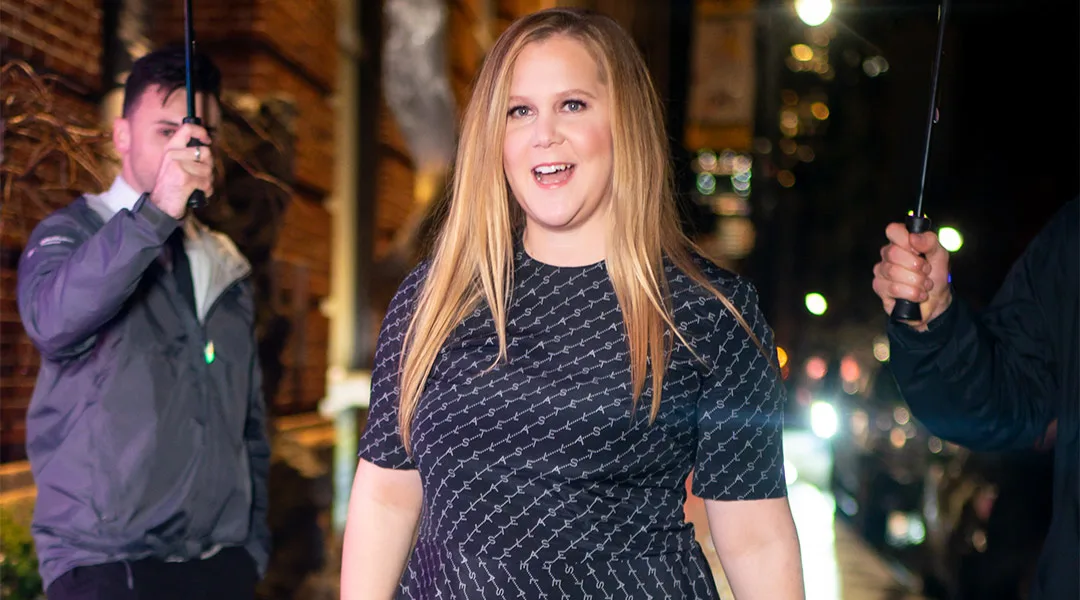 amy schumer walks in rainy city street