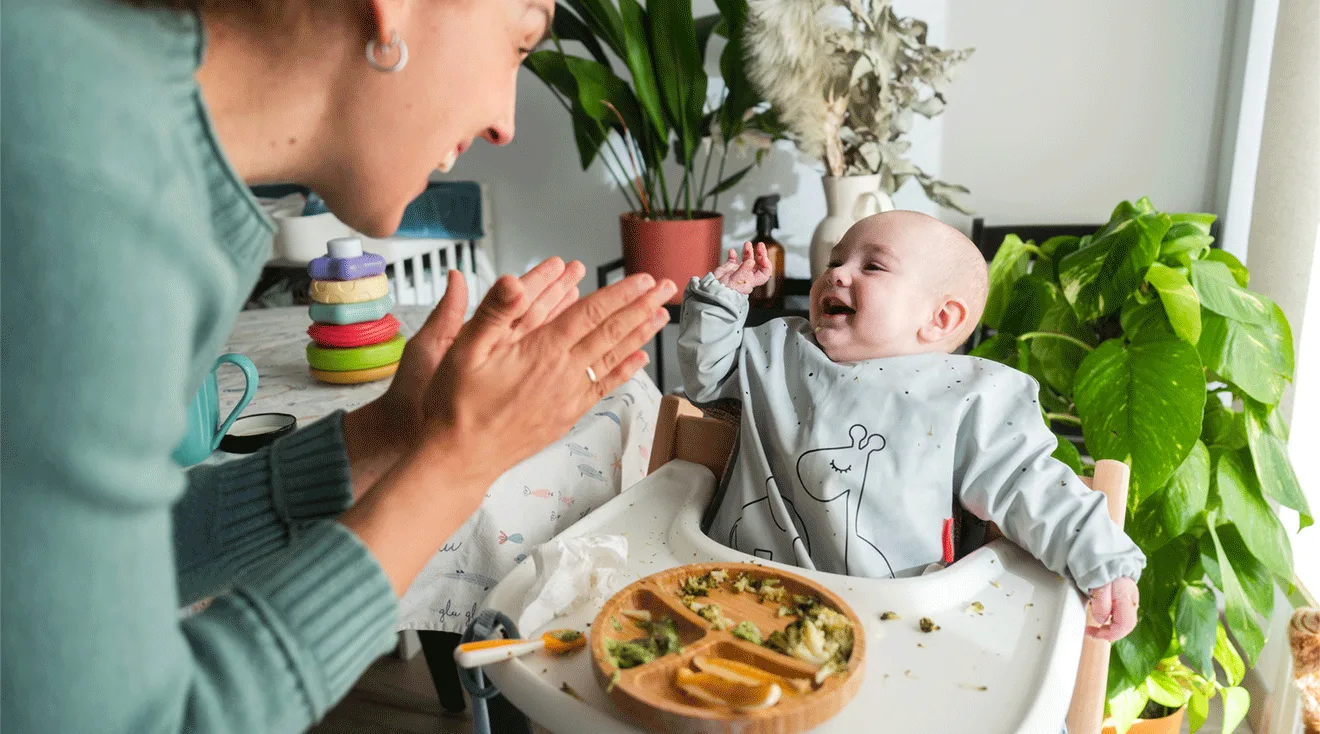 mom clapping for baby while eating food in high chair