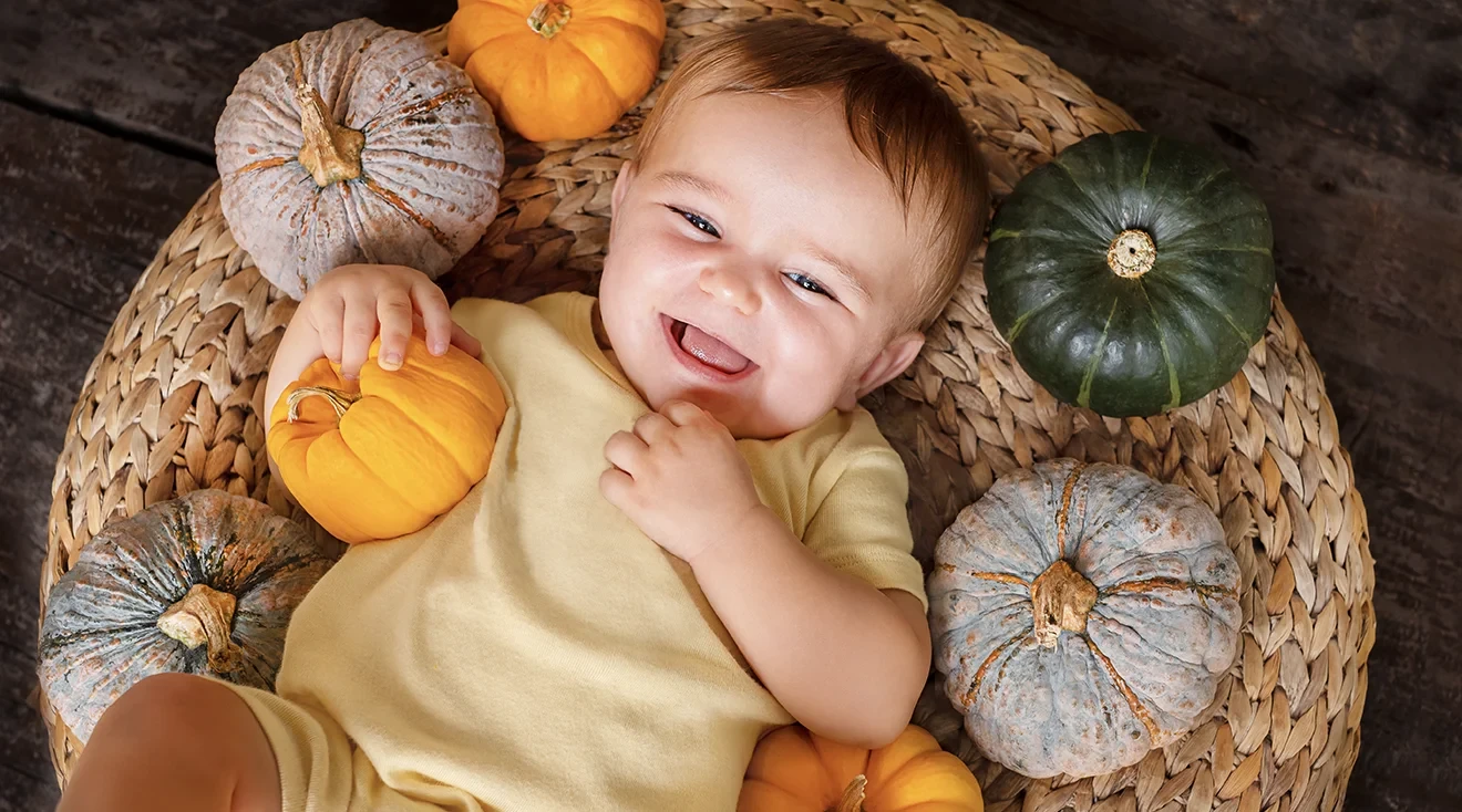 laughing baby surrounded by mini pumpkins for thanksgiving