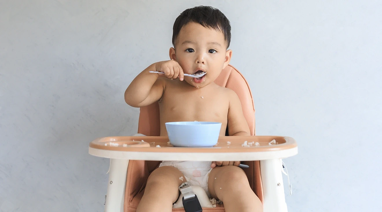 baby sitting in high chair and eating with a spoon