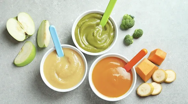 homemade baby food in bowls surrounded by fruits and vegetables