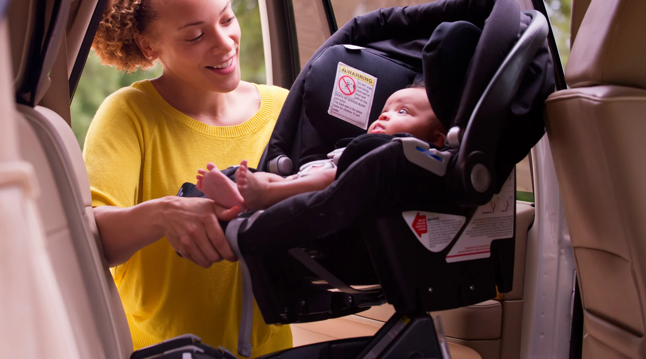 Mom putting newborn baby in car seat into car.