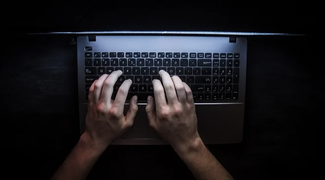 hands on a laptop keyboard in a dark room