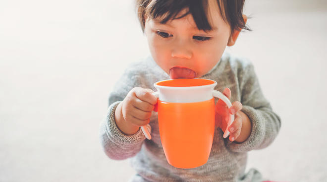 toddler licking orange sippy cup