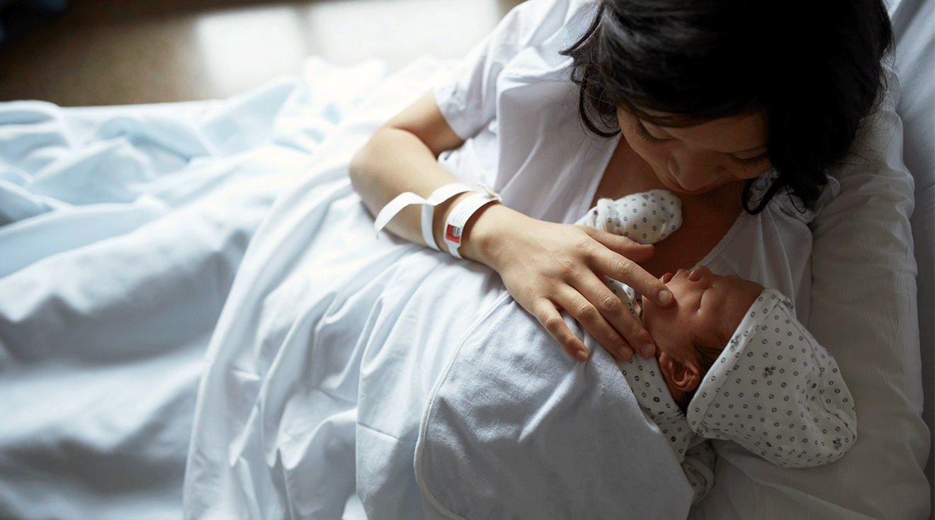 mother touching newborn baby's face in hospital bed after delivery