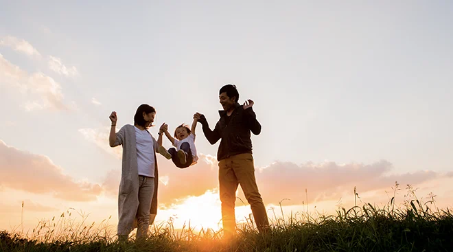 two parents playing with their child outside during sunset