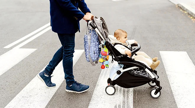 father pushing baby in stroller across crosswalk in city
