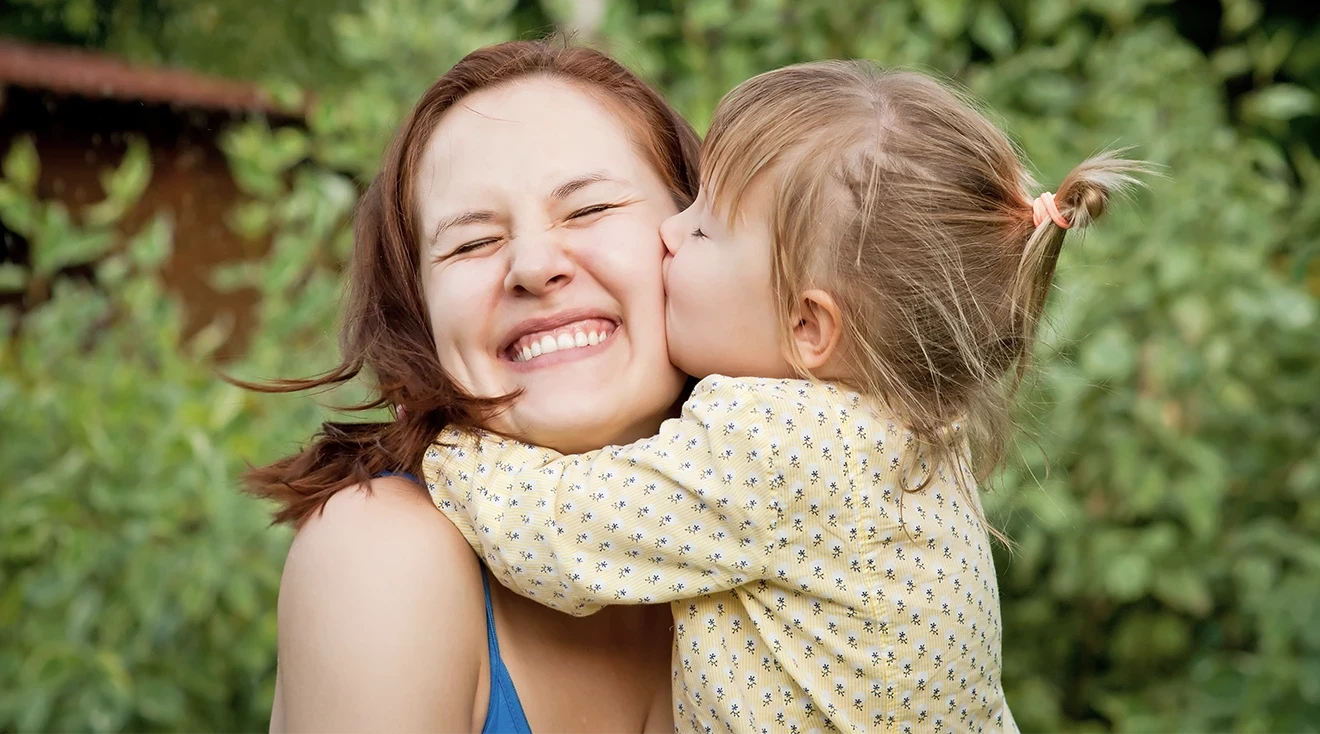 toddler kissing smiling mom on the cheek outside