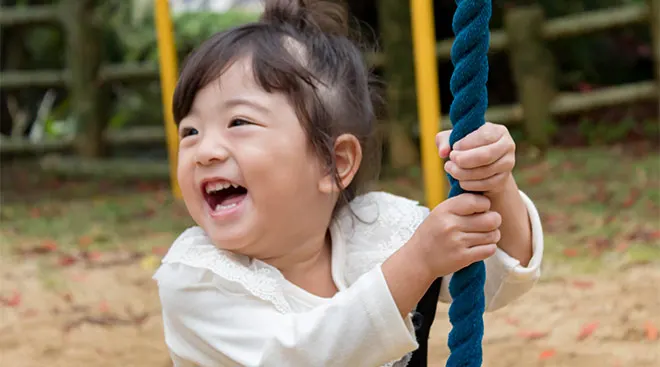Little toddler girl swinging on rope swing at playground.