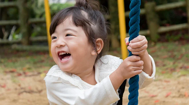 Little toddler girl swinging on rope swing at playground.