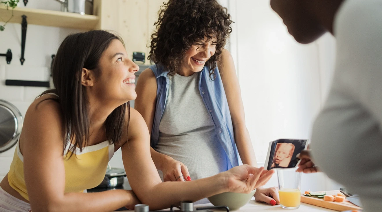 pregnant woman talking and laughing with her friends in kitchen at home