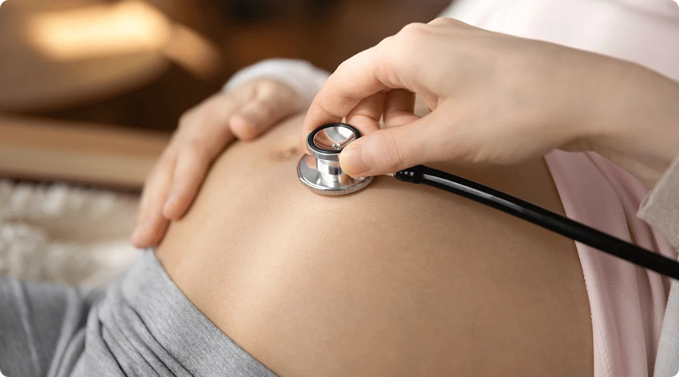 doctor using stethoscope on pregnant belly to hear fetal heartbeat