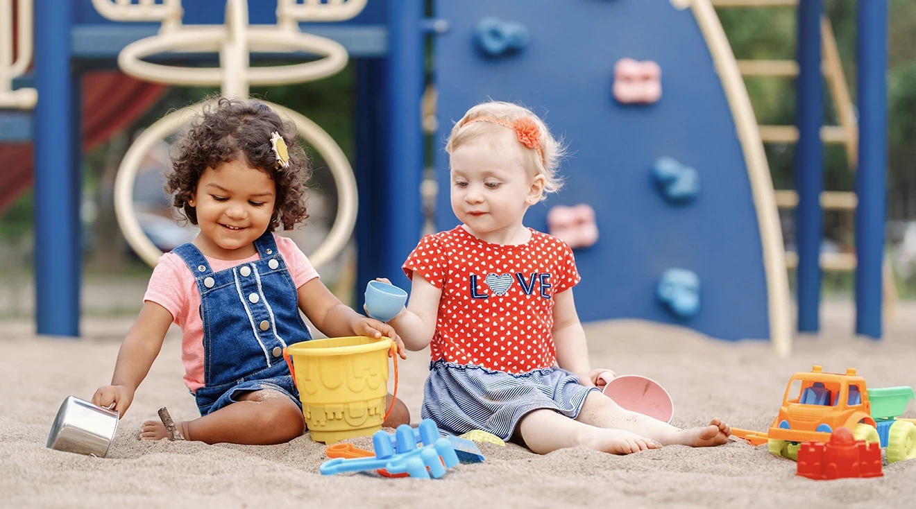 2 toddlers playing in sand at playground