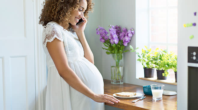 Woman who is late into pregnancy talking on the phone in the kitchen.