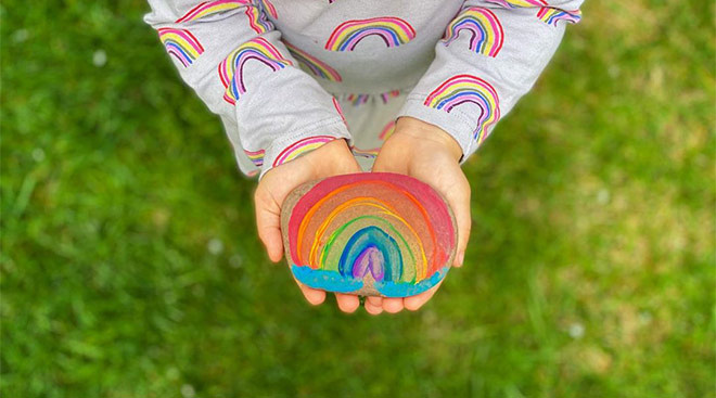 small child holding rainbow painted rock in support of covid-19