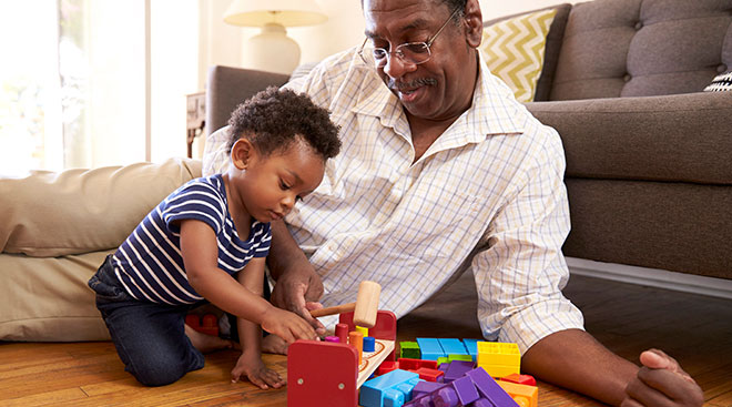 Grandparent playing blocks at home on the floor with his grandchild.