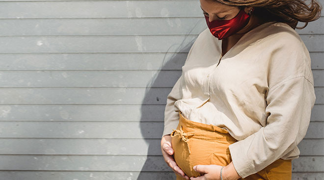 Pregnant woman wearing a face mask and looking down. 