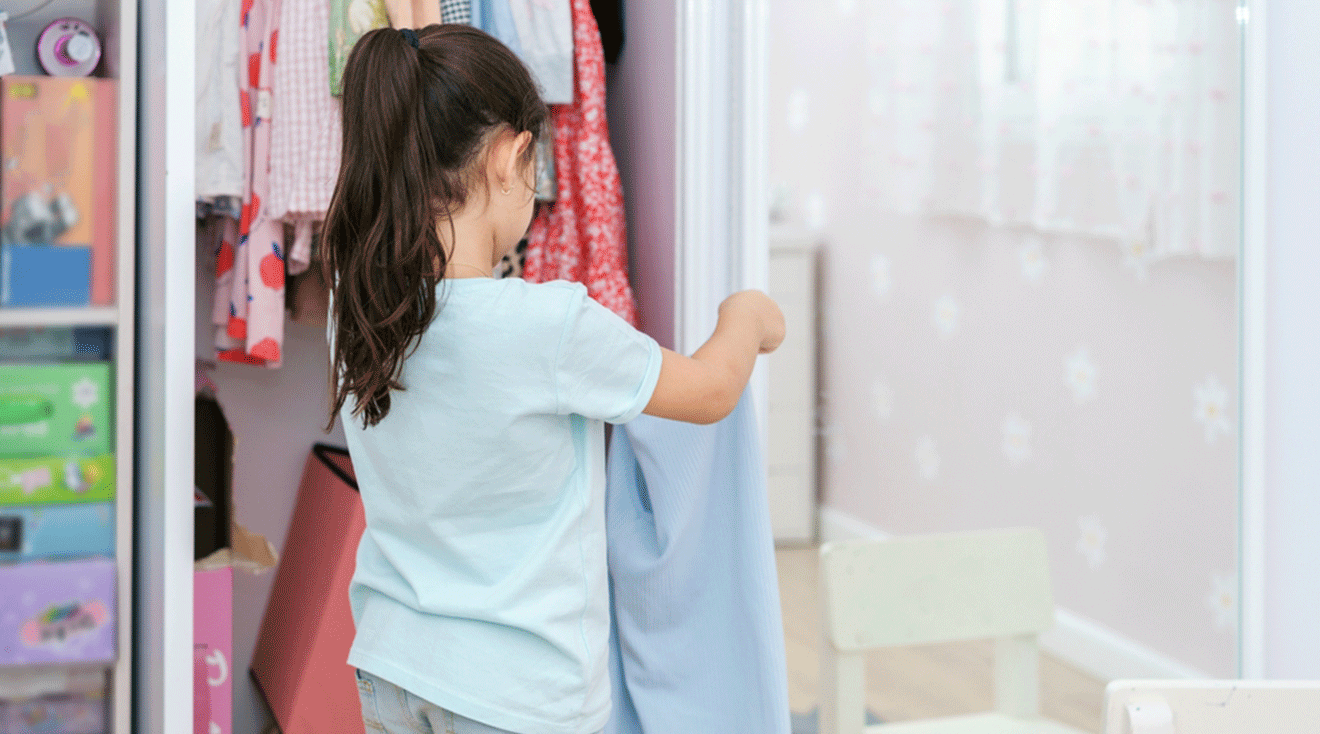 little girl putting clothes away in closet