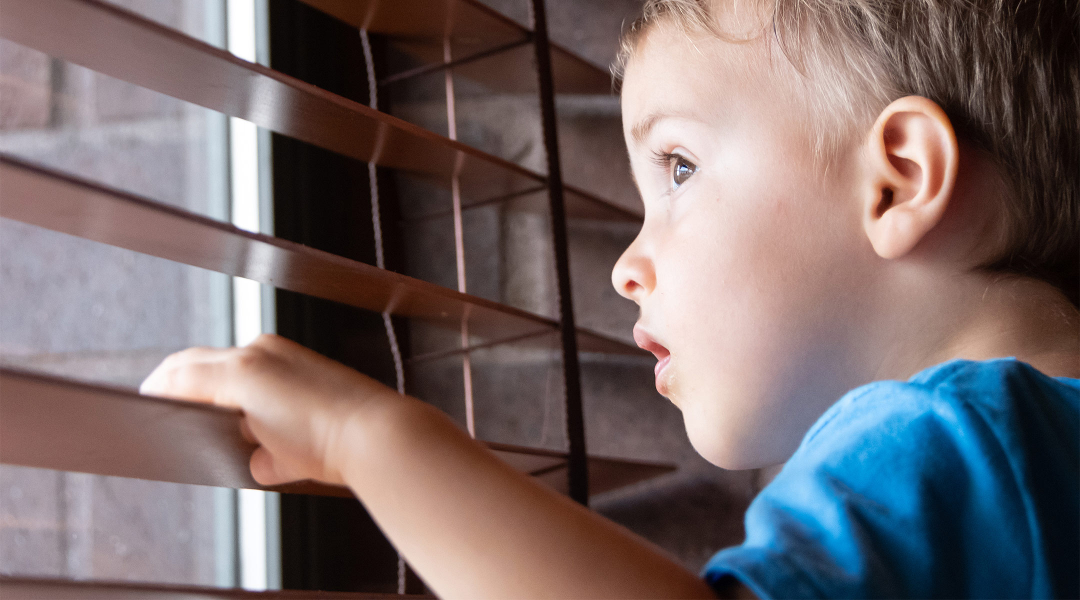 toddler boy looking out window with corded blinds