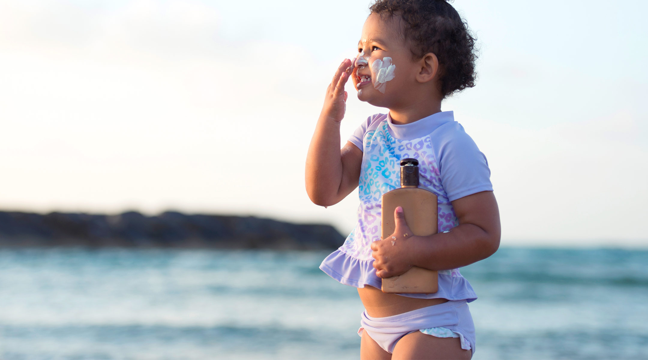 toddler girl puts on sunscreen at the beach