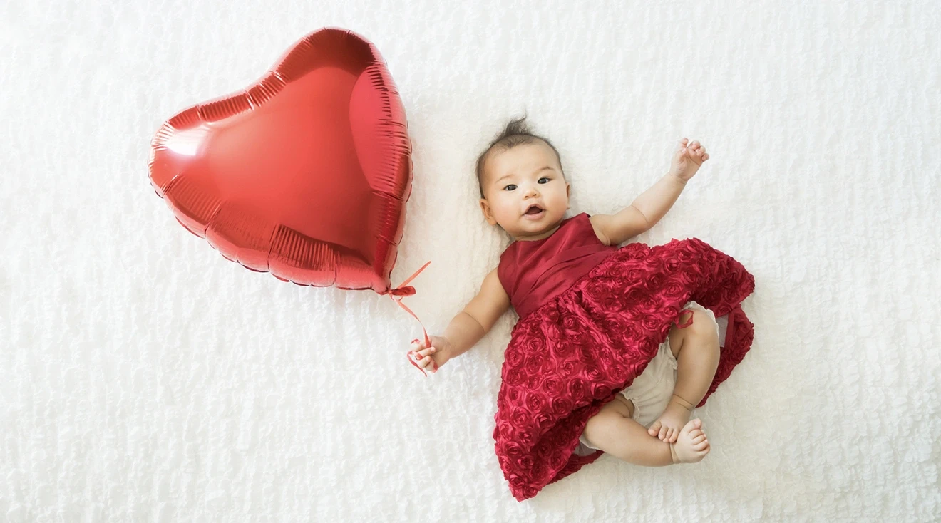 baby in red dress holding a red heart balloon for valentine's day