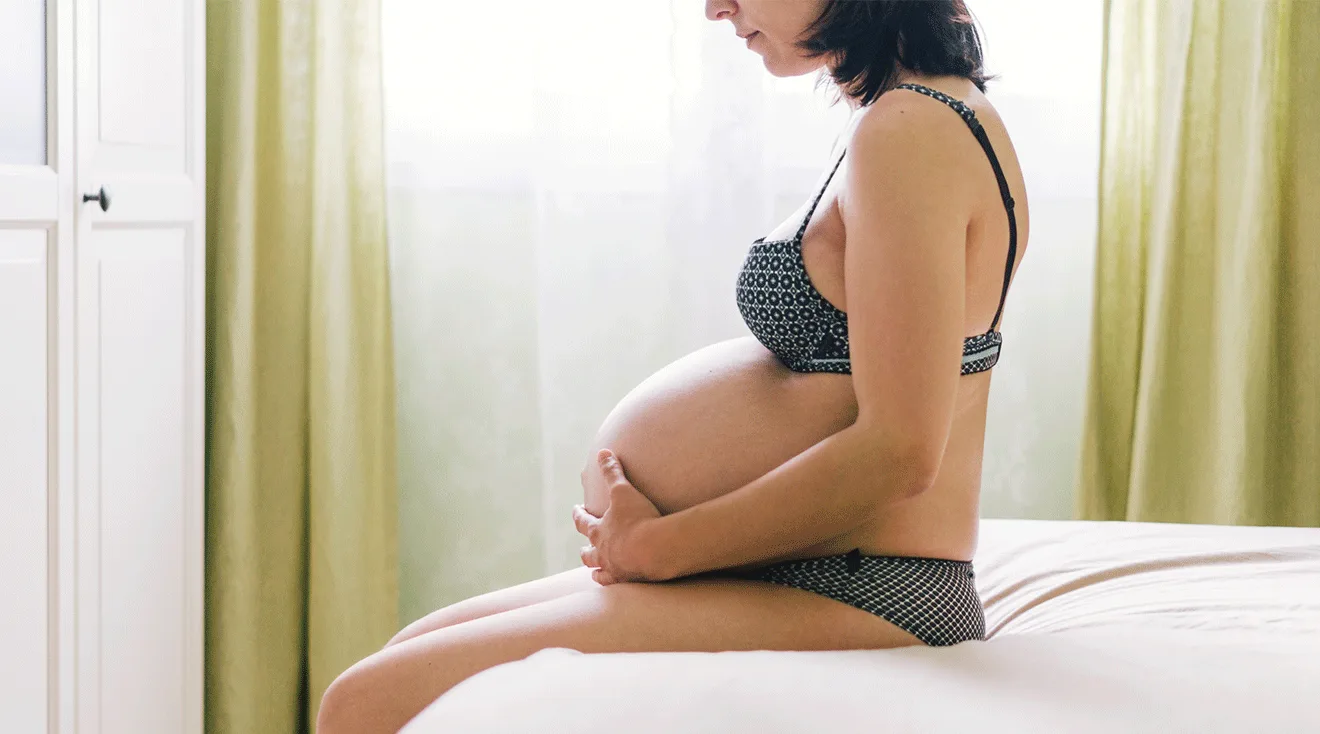 pregnant woman in third trimester sitting on bed