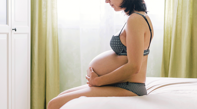 pregnant woman in third trimester sitting on bed