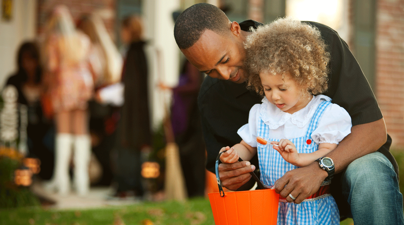 dad helping toddler while trick or treating on halloween