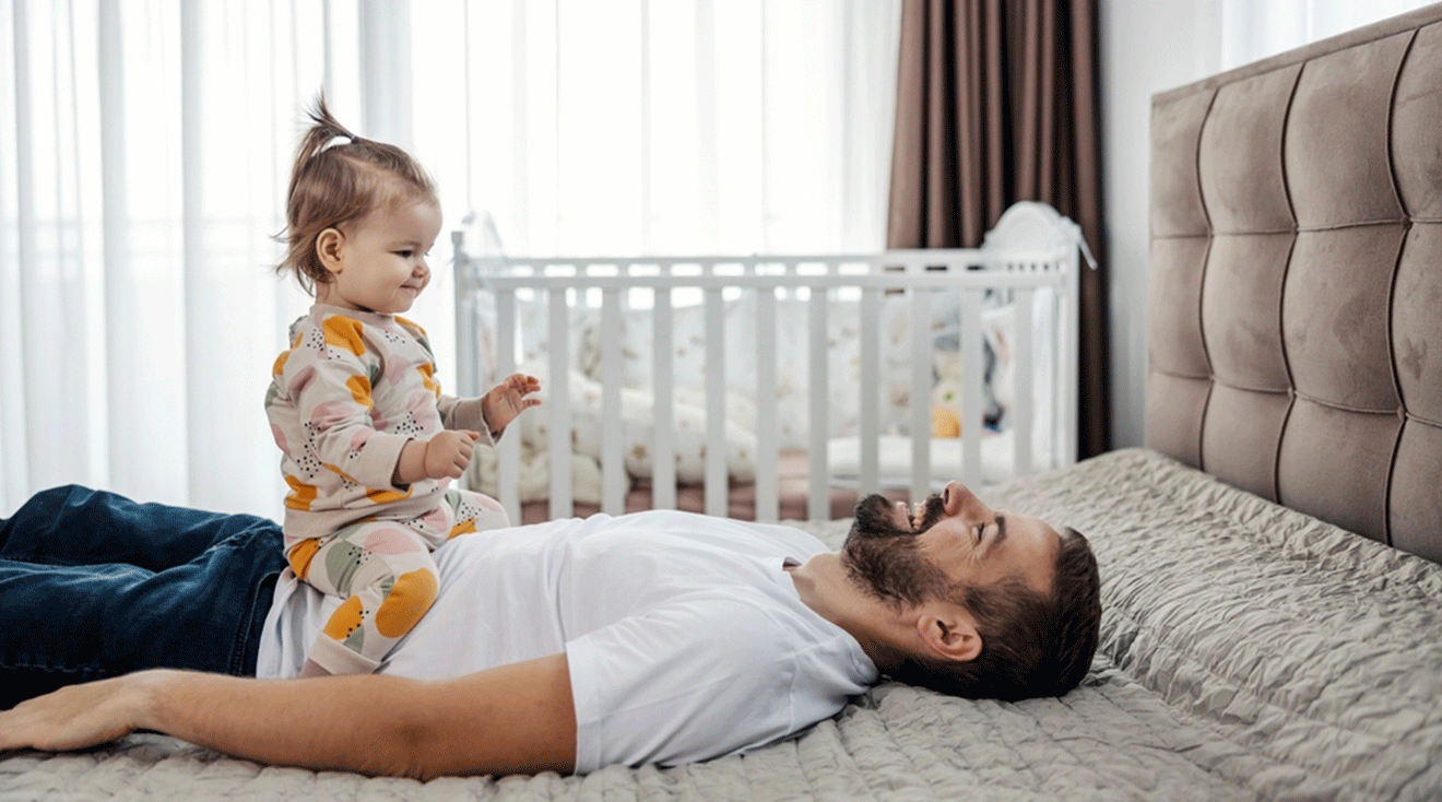 dad playing with toddler daughter while lying down on bed