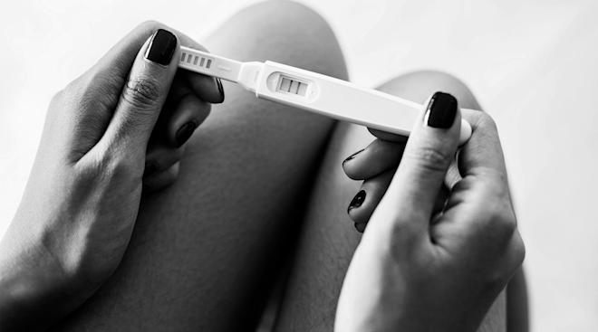 serious woman's hands holding positive pregnancy test