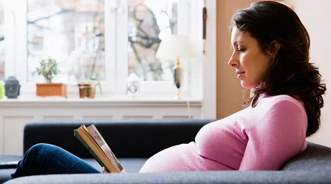 pregnant woman reading a book on the couch at home