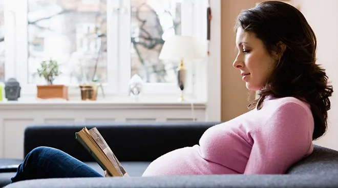 pregnant woman reading a book on the couch at home 