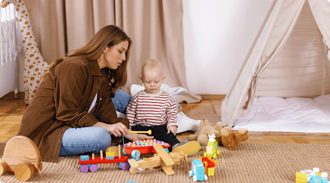 A nanny sitting and playing with baby surrounded by toys.