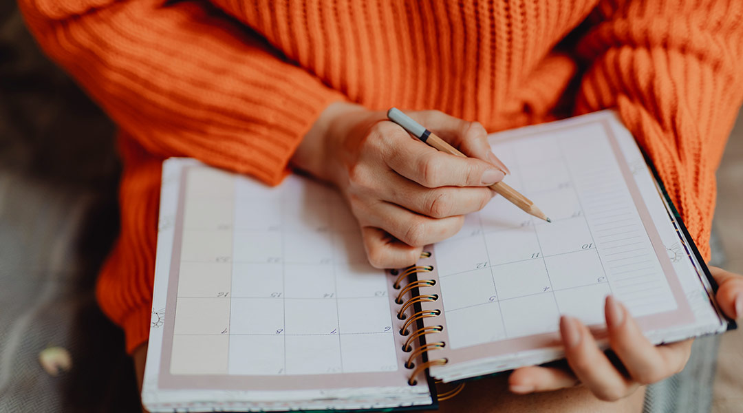 woman in orange sweater making notes in her calendar