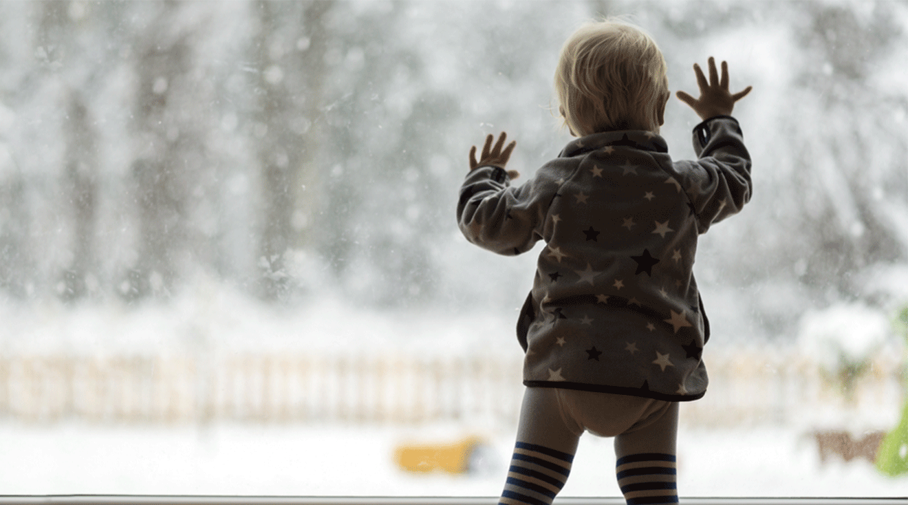 toddler looking out window on a snowy winter day