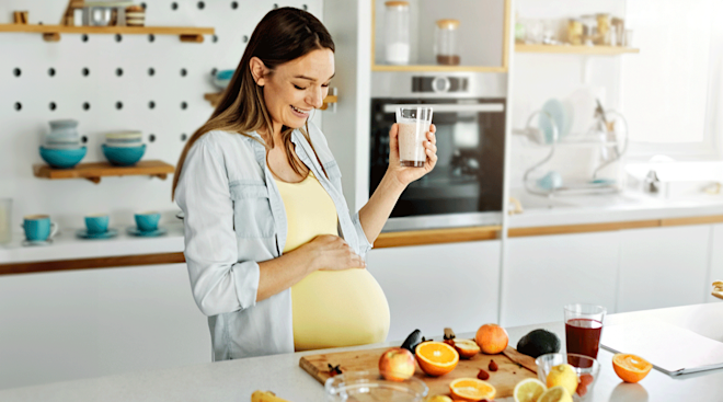 pregnant woman drinking a fruit smoothie in her kitchen at home